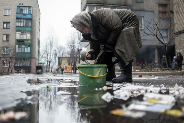 Пожилая женщина собирает воду из лужи в Дебальцево