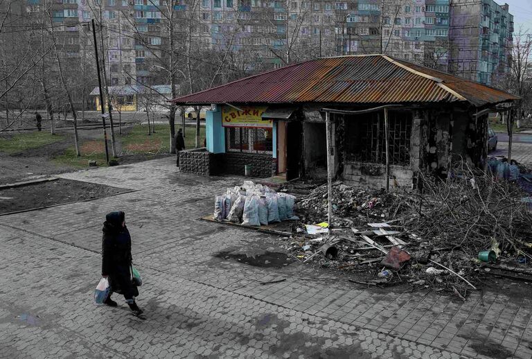 Женщина проходит мимо разрушенной остановки в Мариуполе