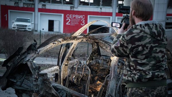 Мужчина снимает автомобиль, сгоревший после обстрела Донецка 4 февраля 2015