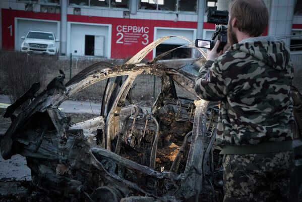 Мужчина снимает автомобиль, сгоревший после обстрела Донецка 4 февраля 2015