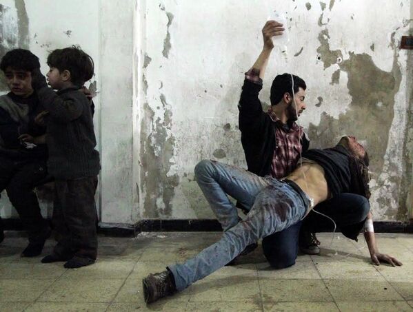 Человек оказывает помощь раненому, пострадавшему во время авиаудара по Сирии