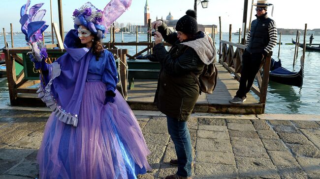Турист фотографирует участницу карнавала недалеко от площади Святого Петра в Венеции