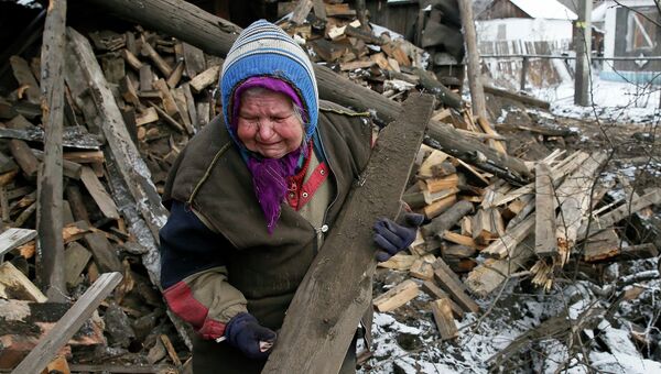 Пожилая женщина разбирает обломки своего дома, пострадавшего от боев в городе Горловка 10 февраля 2015