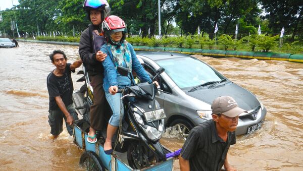 Водитель и пассажир скутера пересекают затопленную дорогу на телеге во время наводнения в Джакарте. Архивное фото