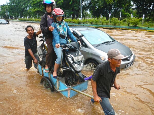 Водитель и пассажир скутера пересекают затопленную дорогу на телеге во время наводнения в Джакарте