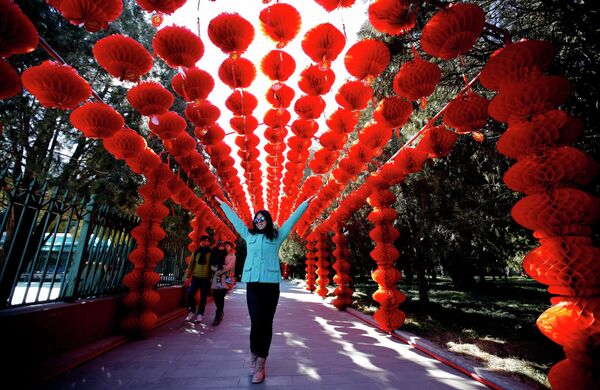 Женщина стоит под традиционными бумажными фонариками в парке Пекина в преддверии празднования китайского Нового года