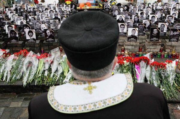 Священник стоит возле фотографий жертв прошлогодних событий на площади Независимости в Киеве