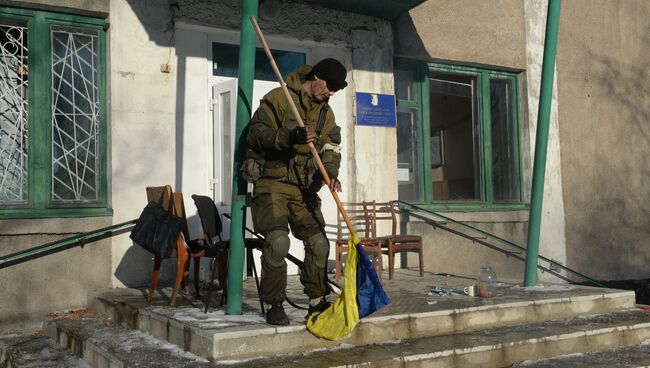 Ополченец Луганской народной республики срывает украинский флаг с древка у входа в поселковую администрацию Чернухино. 20 февраля 2015