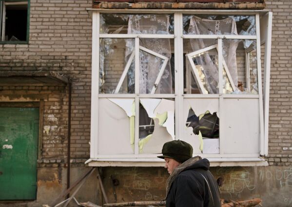 Женщина идет возле поврежденного дома в Дебальцево
