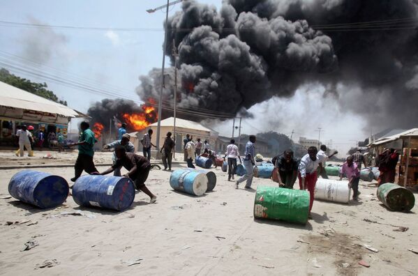 Люди откатывают бочки с горючим от взорвавшейся заправочной станции в Могадишо, Сомали