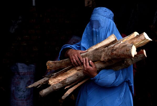 Афганская женщина несет купленные дрова в свой дом в Герате