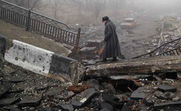 Пожилая женщина идет по разрушенному мосту возле аэропорта Донецка, Украина