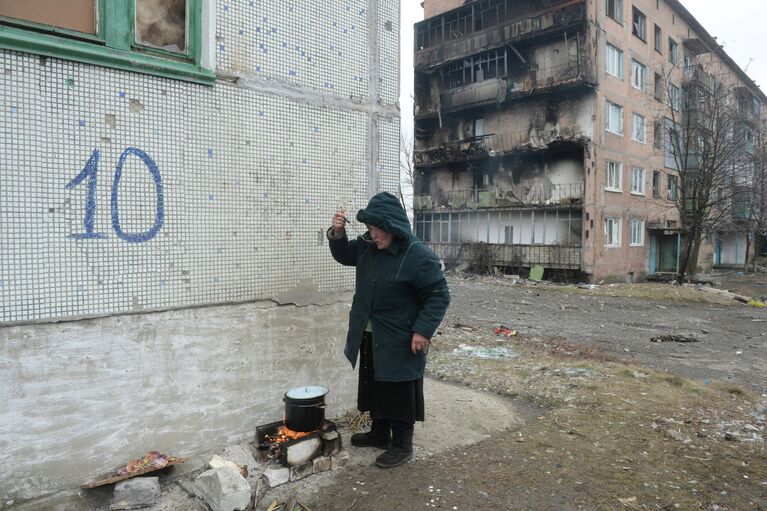 Жительница города Дебальцево готовит еду на костре на улице у жилого многоквартирного дома, пострадавшего в результате обстрелов во время боевых действий