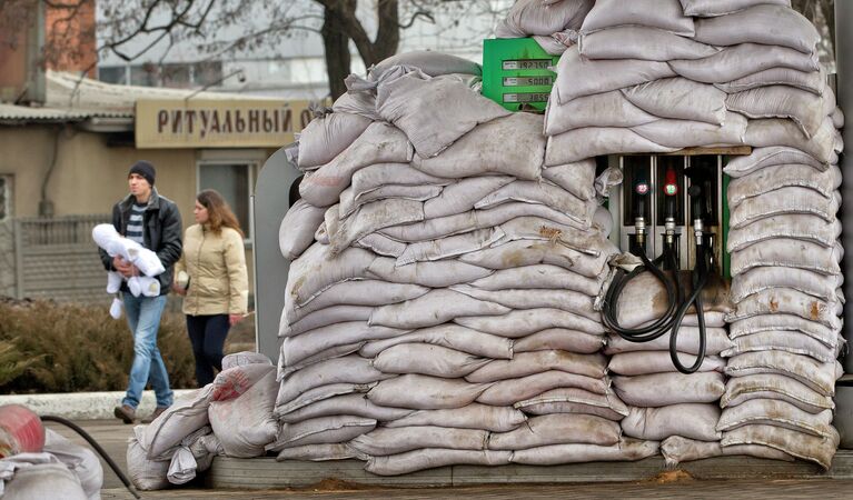 Молодая семья проходит мимо топливного насоса, покрытого мешками с песком от возможного обстрела. Донецк, Украина