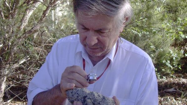 Профессор Гликсон изучает образец породы, сжатой и переплавленной в ходе падения астероида