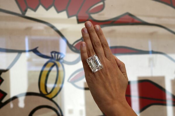 Женщина показывает кольцо с редким бриллиантом изумрудной огранки, весом в 100,2 карата, на фоне картины Роя Лихтенштейна на предпоказе аукциона Sotheby's 25 марта 2015, Лос-Анджелес