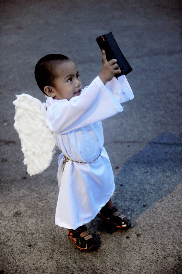 Ребенок одетый ангелом принимает участие в религиозной процессии на Пасху в пригороде Манилы