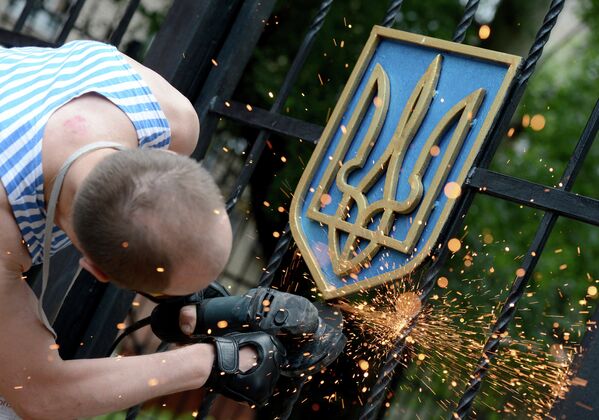 Боец ополчения Луганской народной республики срезает герб Украины с ворот здания областной администрации в Луганске