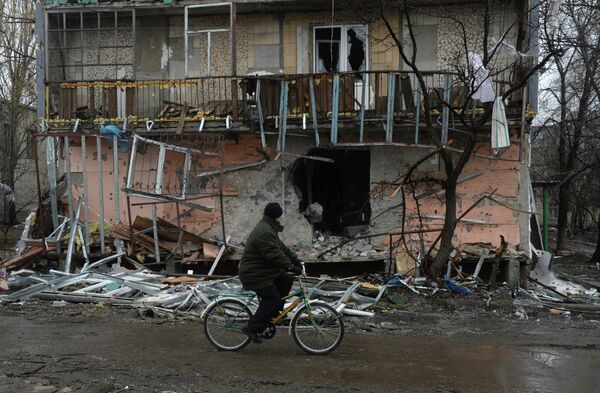 Житель города Дебальцево едет на велосипеде мимо разрушенного в результате обстрелов во время боевых действий жилого дома