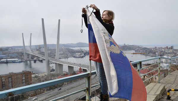 Женщина повязывает траурную ленту на флаг РФ во Владивостоке в память о погибших в Охотском море при крушении траулера Дальний Восток. Апрель 2015