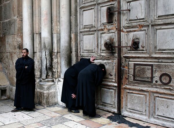 Священнослужители наблюдают через отверстия в дверях церкви Гроба Господня за церемонией схождения Благодатного Огня в  в Иерусалиме 11 апреля 2015