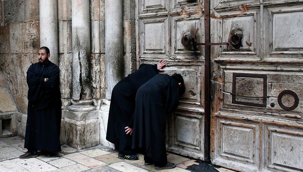 Священнослужители наблюдают через отверстия в дверях церкви Гроба Господня за церемонией схождения Благодатного Огня в  в Иерусалиме 11 апреля 2015