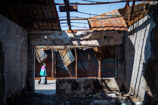Женщина несет ее покупки мимо сгоревших рыночных прилавков в Донецке