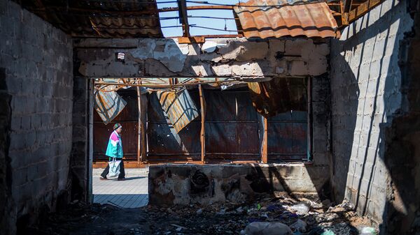 Женщина несет ее покупки мимо сгоревших рыночных прилавков в Донецке. Архивное фото