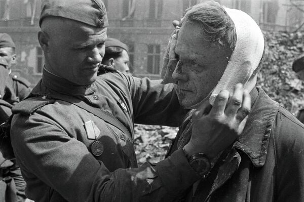 Советский солдат делает перевязку раненому в голову берлинцу