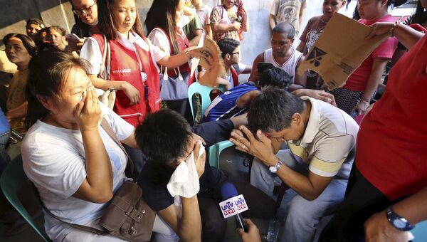 Родственники пострадавших во время пожара на фабрике по производству сандалий в столице Филиппин Маниле. 13 мая 2015