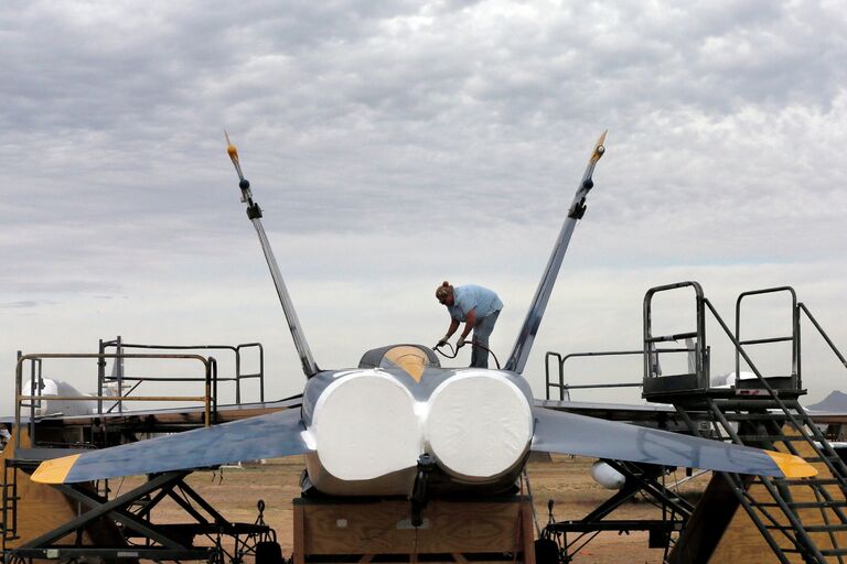 Военнослужащий покрывает водонепроницаемой краской американский истребитель-бомбардировщик F-18 на авиабазе ВВС США Девис-Монтен в Тусоне, Аризона