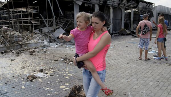 Женщина с ребенком проходит мимо рынка, разрушенного в результате обстрелов, в Донецке