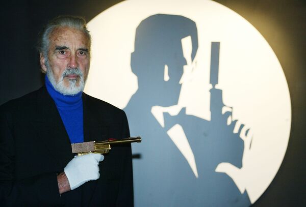 Актер Кристофер Ли держит золотой пистолет на открытии выставки о Джеймсе Бонде