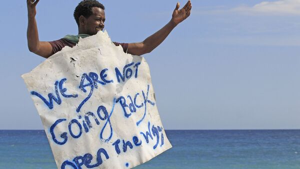 Мигрант держит плакат с надписью Мы не собираемся обратно на границе Франции и Италии в городе Вентимилья