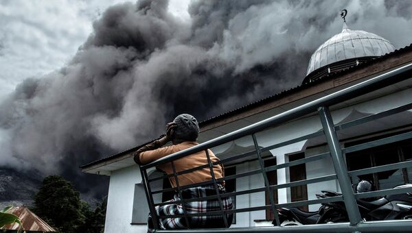 Женщина наблюдает за извержением пепла из вулкана Синабунг в провинции Северная Суматра. Июнь 2015