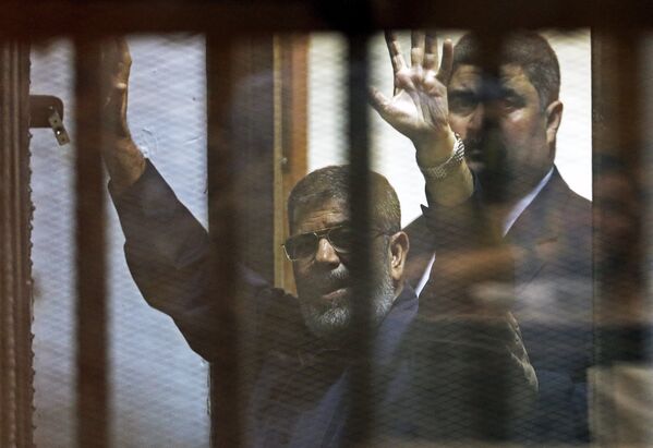 Свергнутый президент Египта Мохаммед Мурси приветствует своих юристов и людей из-за решетки