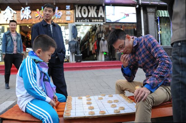 Мальчик и мужчина играют в Сянцы (китайские шахматы) на одной из улиц Маньчжурии