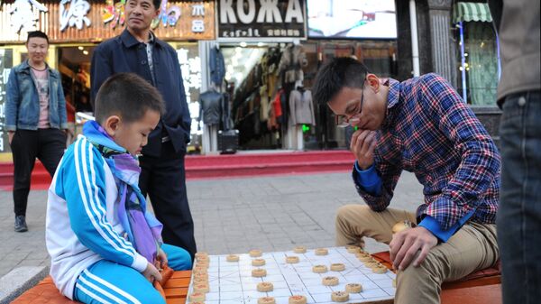 Мальчик и мужчина играют в Сянцы (китайские шахматы) на одной из улиц Маньчжурии