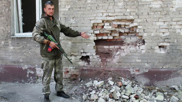 Ополченец показывает пробоину в стене жилого дома от попадания снаряда ВС Украины. Архивное фото