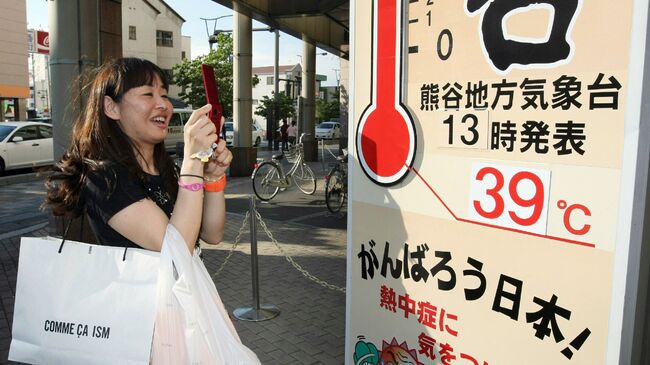 Женщина фотографирует термометр на улице в Кумагая, Япония. Архивное фото