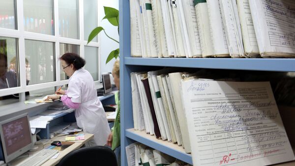 Медицинский работник выдает медицинскую карту пациенту в регистратуре поликлиники. Архив