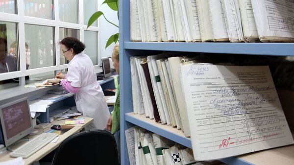 Медицинский работник выдает медицинскую карту пациенту в регистратуре. Архивное фото