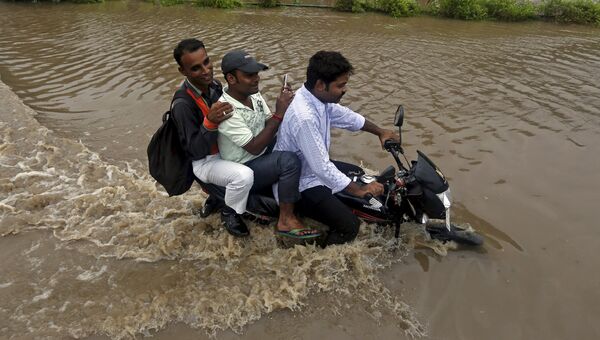 Мужчины едут на мотоцикле по затопленной дороге после проливных дождей в Ахмедабаде, Индия
