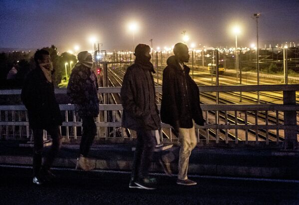 Мигранты пересекают мост над железнодорожными путями Евротуннеля в городе Кале