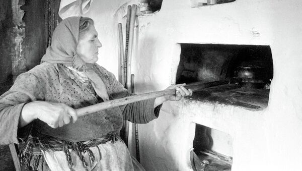 В украинском селе.  Женщина ставит горшки в печь ухватом