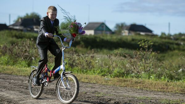 Мальчик с цветами едет на велосипеде в школу. Архивное фото