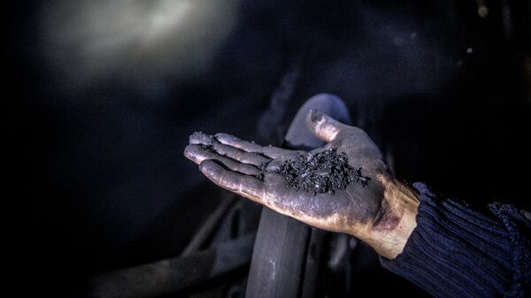 Шахтер показывает уголь на шахте. Архивное фото