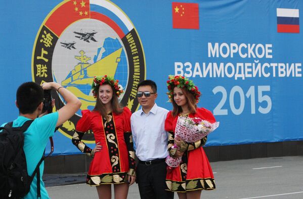 Участник китайской делегации фотографируется с русскими девушками на фоне баннера совместных учений Морское взаимодействие - 2015