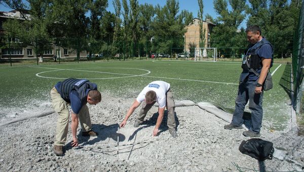 Сотрудники миссии ОБСЕ изучают воронку от разорвавшегося снаряда на территории школы № 16 в Горловке