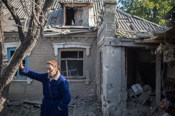 Женщина у поврежденного в результате обстрела дома в поселке Александровка 